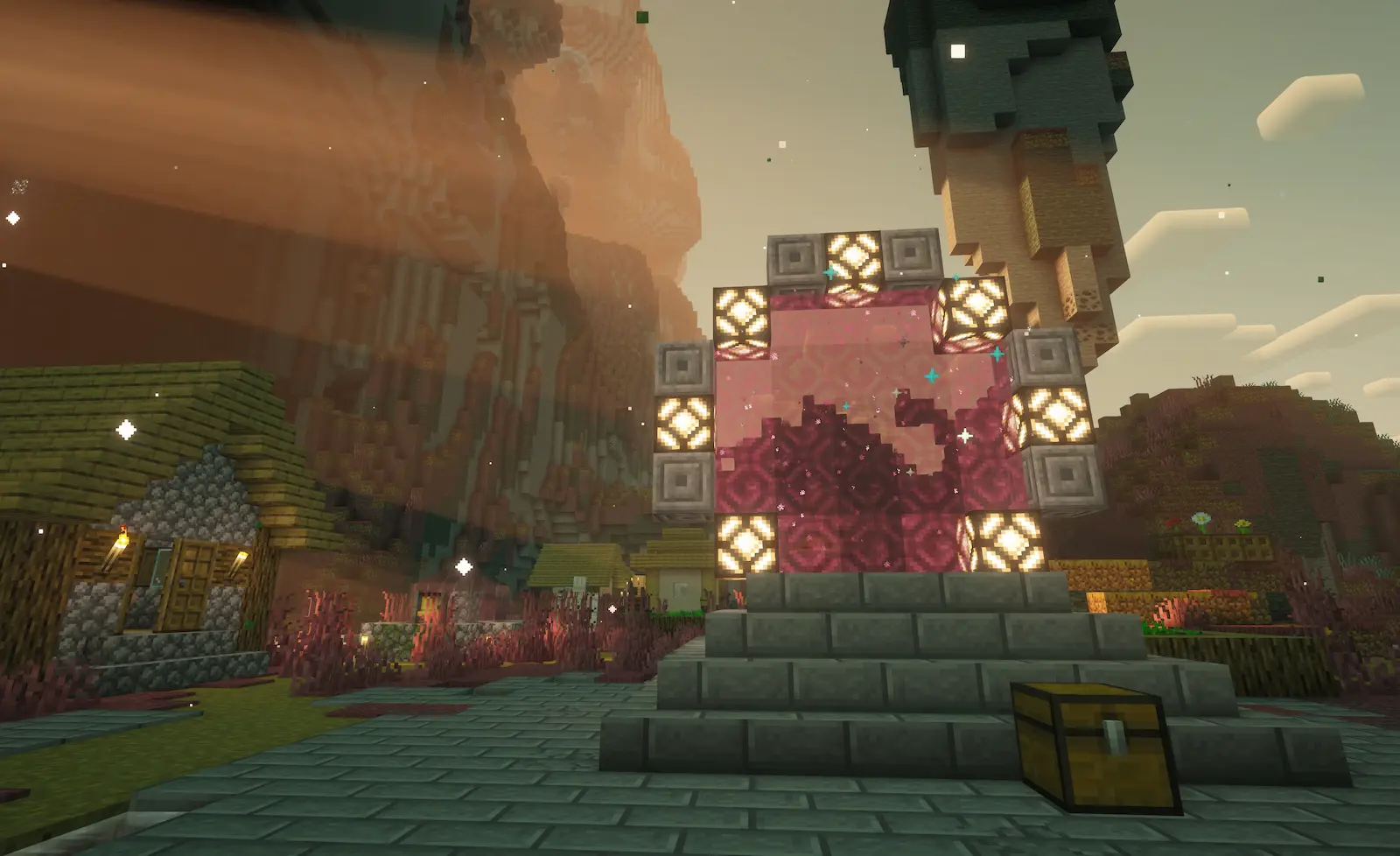 A coral-pink Stargate on stone steps beside a village of thatched houses, under a towering rose-coloured mesa and a peach sky